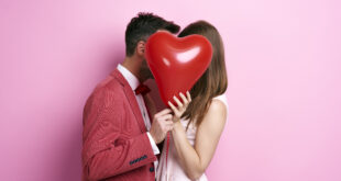 affectionate couple covering face with balloon kissing