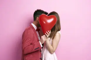 affectionate couple covering face with balloon kissing