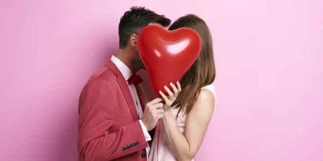 affectionate couple covering face with balloon kissing