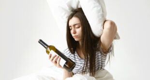 stressed unhappy woman with messy loose hair suffering from headache after party holding pillow empty bottle