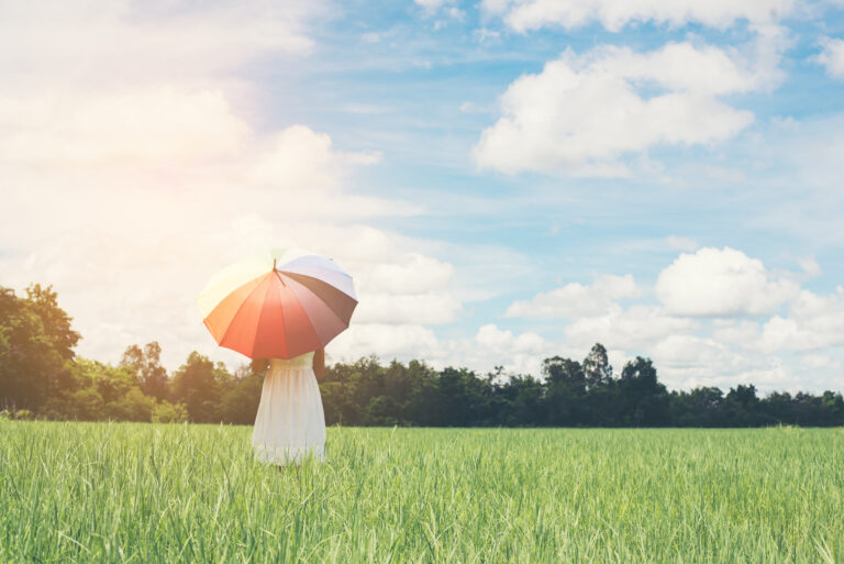 Back Of Young Beautiful woman holding multicolored umbrella in g