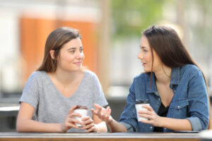 Two friends talking in a park drinking coffee